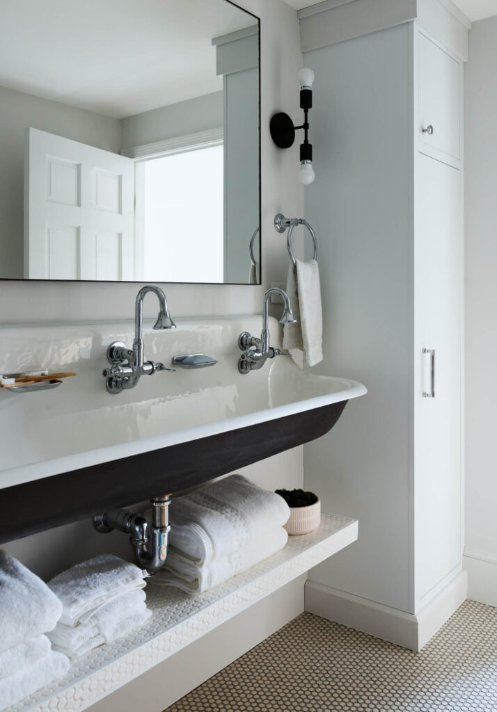 Kid-friendly black-and-white bathroom with a trough sink, penny tile floor, custom cabinet, and simple lighting in Hingham by a Boston-area interior designer.