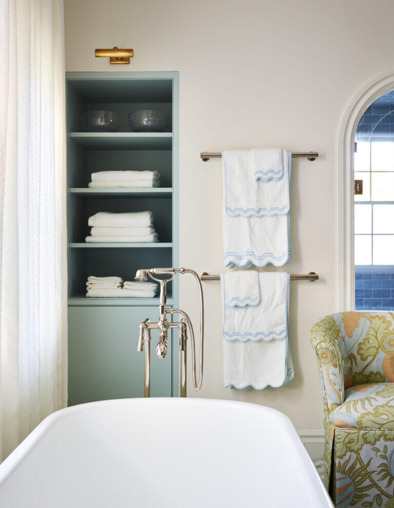 Custom light blue painted shelf, freestanding tub with tub filler, and a small slipper chair in a Milton bathroom renovation.