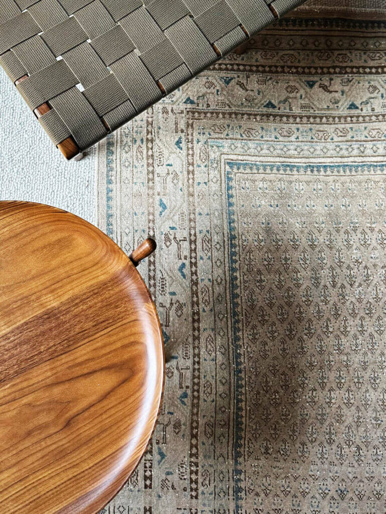 A vintage area rug layered on off-white carpet in a Vermont family room with a woven Risom chair and a custom walnut side table.