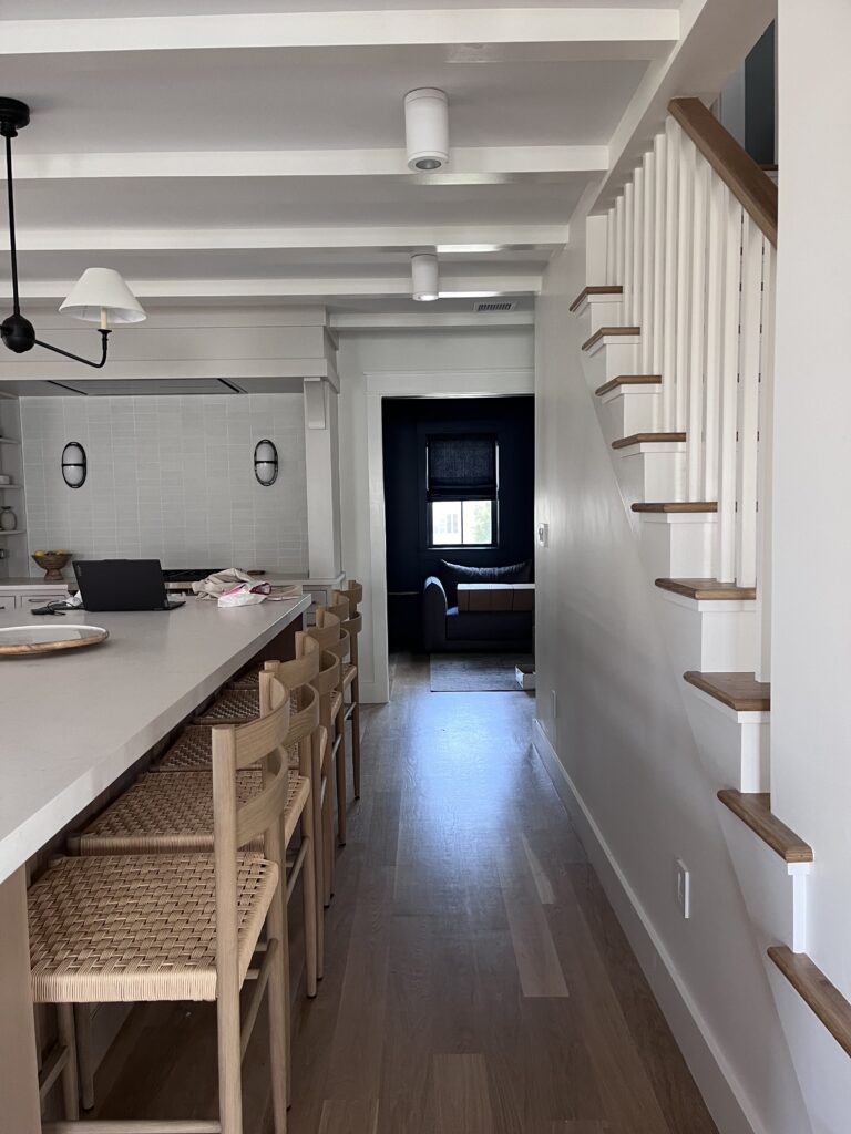 Custom kitchen with faux beams, neutral cabinets, tile backsplash, and unique lighting in a beach house by a Boston kitchen designer.