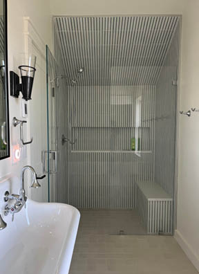 Kids bunk room bathroom with off-white floor tile, striped wall tile, and wall-mounted sink in a South Shore beach house by a Boston interior decorator.