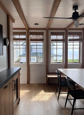 Sun porch with white shiplap walls, natural wood beams and posts, and custom cabinets at a South Shore beach home by a Boston-area interior designer.