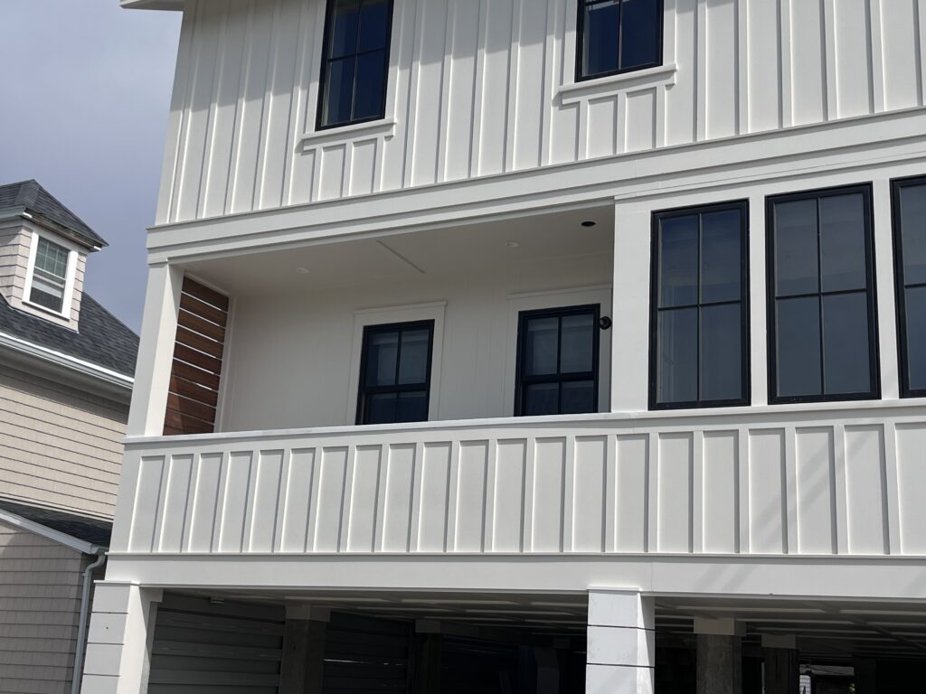 Coastal exterior design with white board and batten siding and black windows for a new construction beach house by architect Owen Thomas.