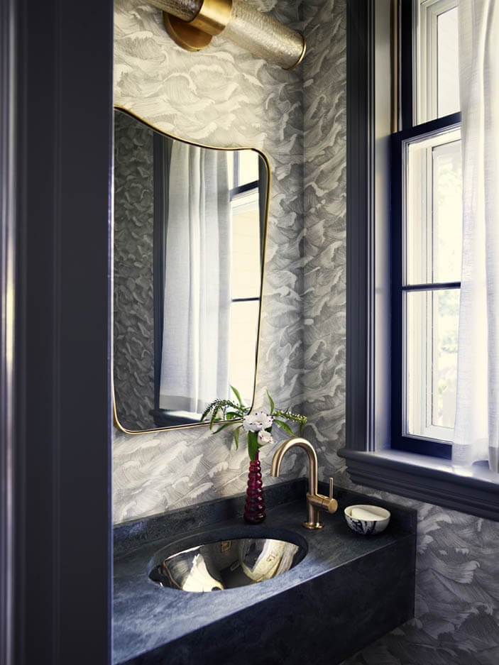 Powder room with grey Cole & Son Waves wallpaper, soapstone sink, brass fixtures, and a soft white café curtain. Designed by Boston interior decorators.