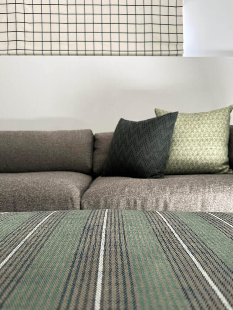 A custom green striped ottoman with Zak & Fox fabric, a black Blu Dot sectional, and plaid Roman shades in a Vermont ski house basement media room.