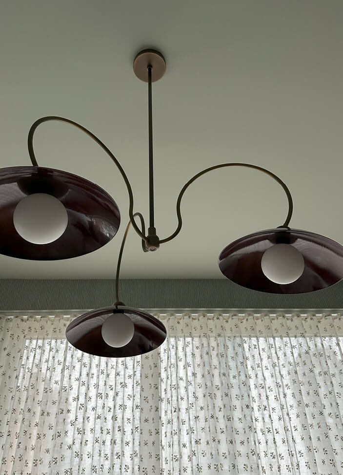 A custom burgundy chandelier from Blueprint Lighting, Zak and Fox wallpaper, and Cowtan and Tout drapery panels in the primary bedroom of a NYC apartment.