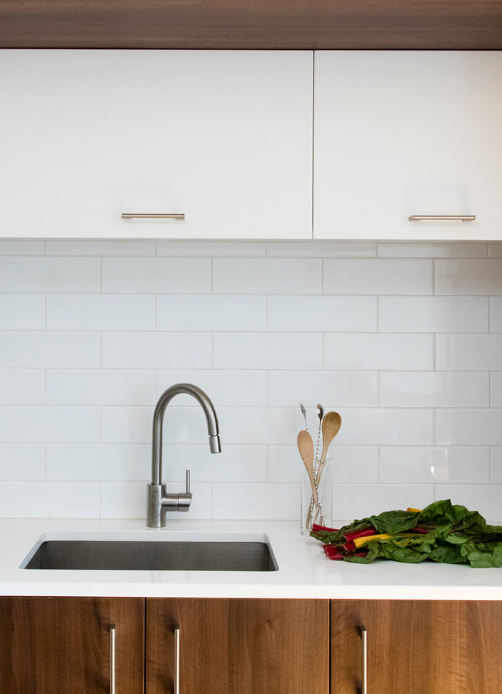 A modern South Boston loft kitchen with white cabinets, walnut accents, a simple white counter, and a sleek white backsplash.