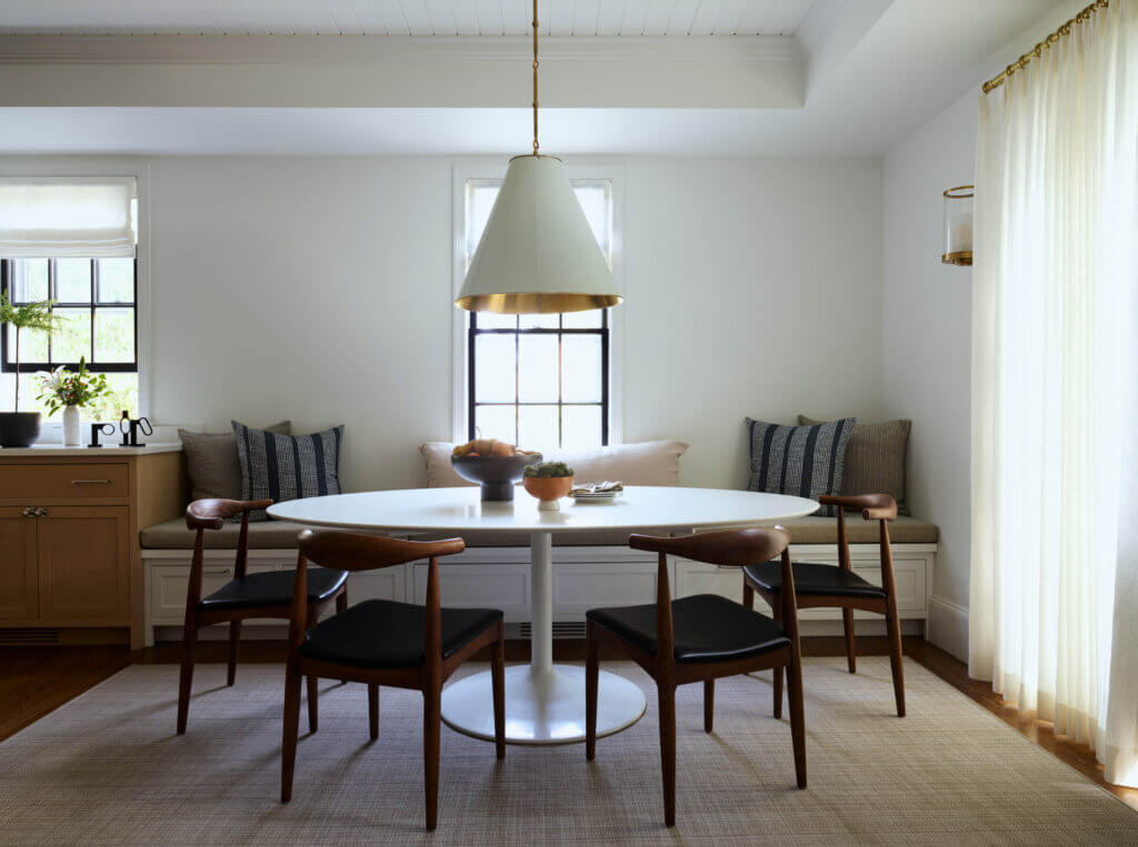 A modern dining space in a historic Hingham home with a custom bench, mid-century furniture, and a white and brass pendant light.