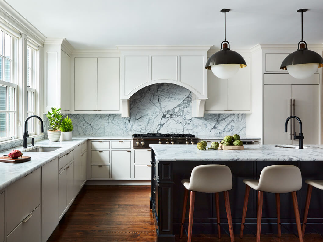 A sleek Boston kitchen design with white slab cabinets, a black island, Carrera marble counters, and Allied Maker pendant lighting.