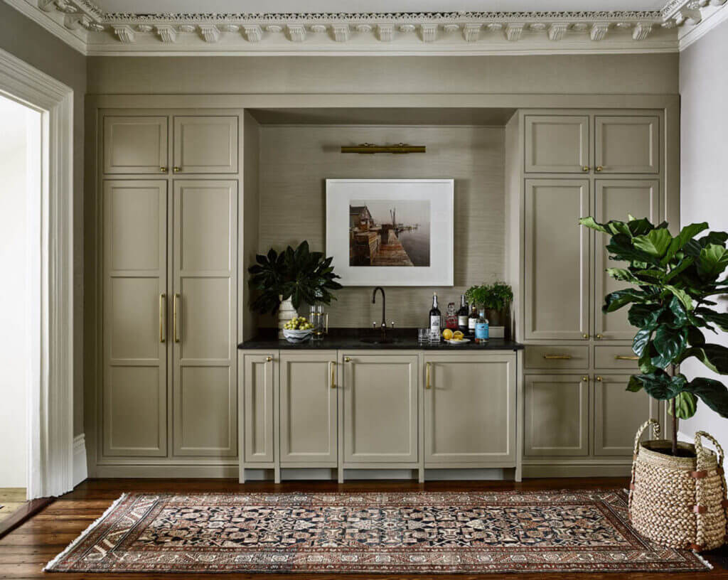 A Boston kitchen designer created custom beige cabinets with a sink, fridge, and tall storage for coats and dining essentials in a historic brownstone.