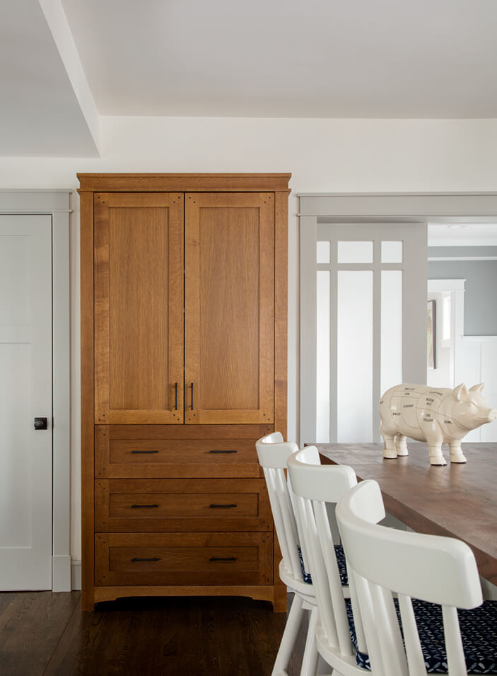 A South Boston kitchen with custom fumed oak cabinets, a walnut island counter, white walls, light grey trim, and simple white stools.