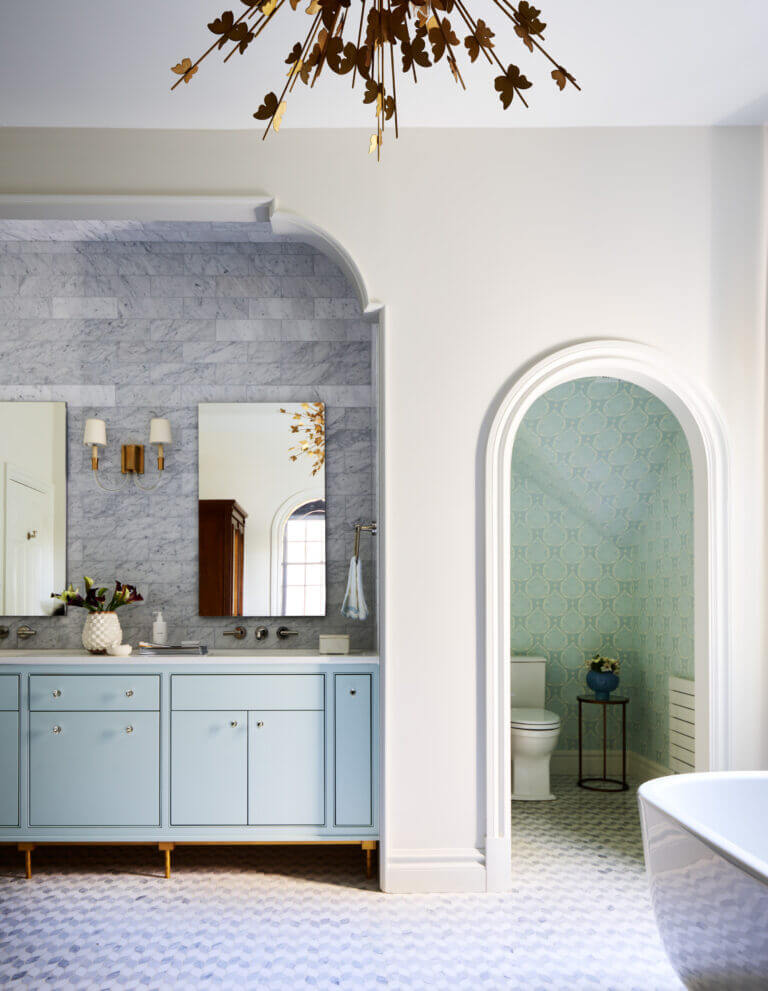 Full-Service Design Boston for a custom primary bathroom featuring light blue cabinets, marble backsplash, a curved niche, and a freestanding tub.