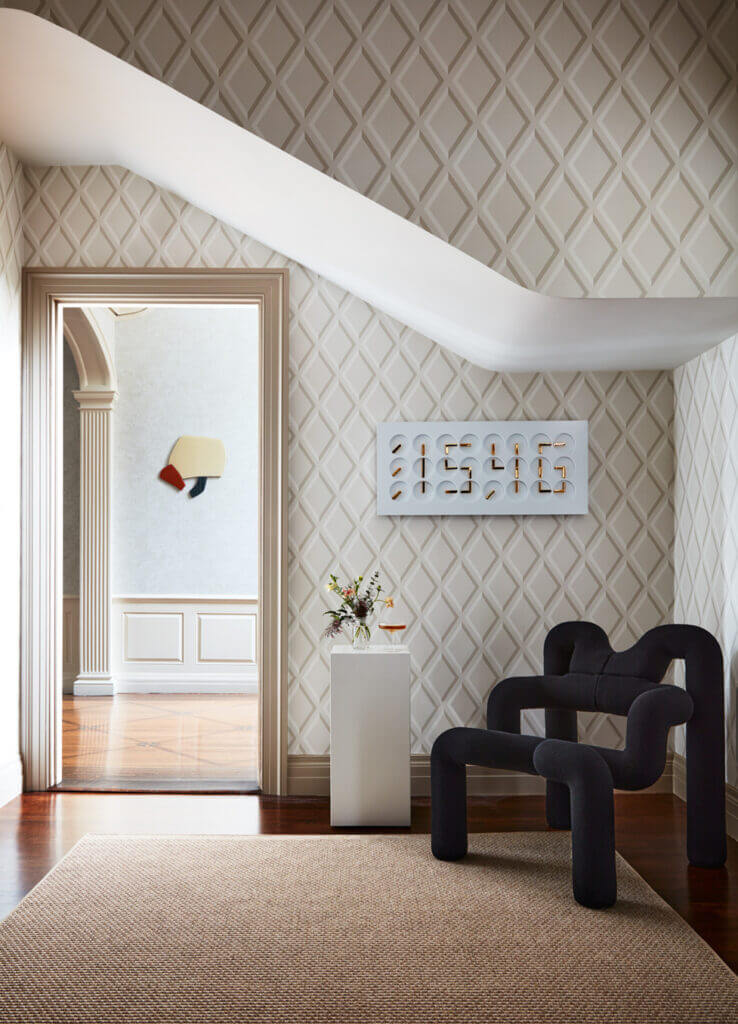 A Boston corridor with geometric wallpaper, traditional trim, a modern black chair, custom digital clock art, and a neutral area rug for a balanced, contemporary design.