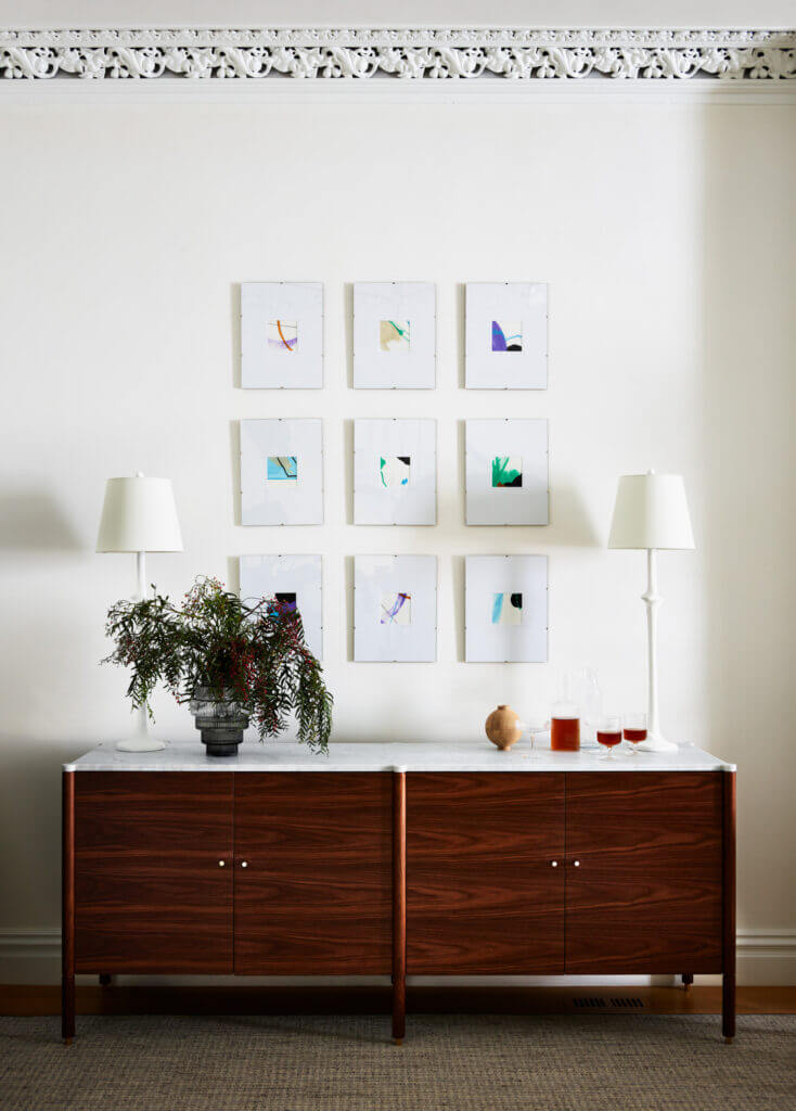 A walnut and marble console with brass hardware, geometric artwork, and plaster white buffet lamps, creating a cohesive and elegant design.