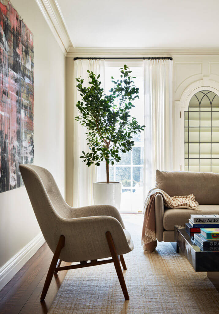 Historic Home Interior Design in a formal living room featuring a Scandinavian upholstered chair, fine art, white linen drapery panels, and original millwork with leaded glass built-ins.