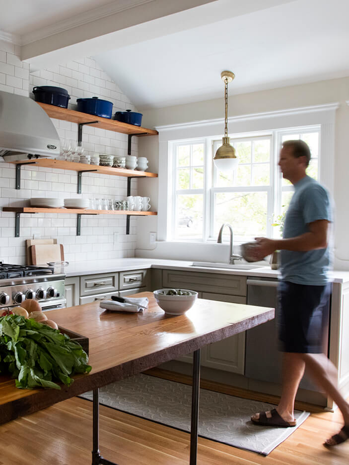 A classic Boston kitchen design in a Winchester home with light green cabinets, reclaimed oak shelving, and a locally made wood and metal island.