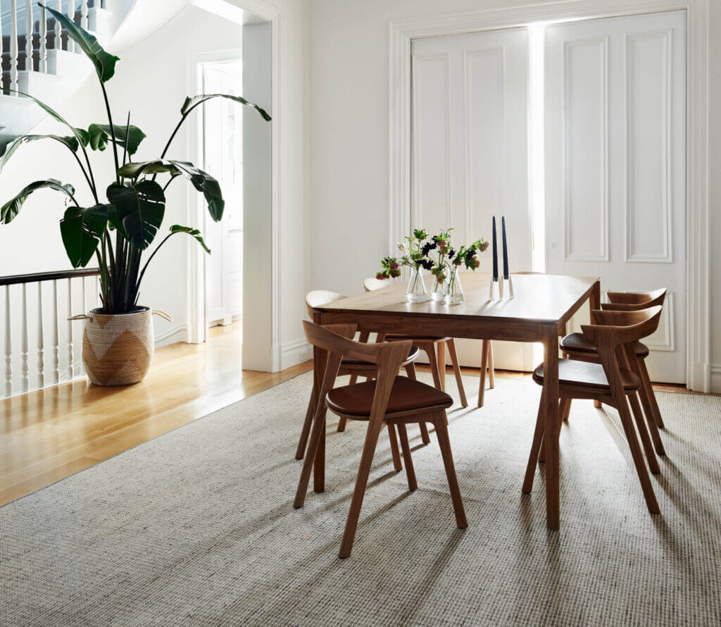 A moody dining space with original doors, soft shadows, a neutral houndstooth rug, and Scandinavian-inspired Bok table and chairs.