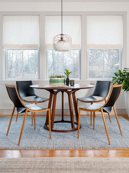 A modern walnut dining table with four leather chairs and a Roll & Hill light fixture, showcasing essential furniture placement in a full home furnishing guide.