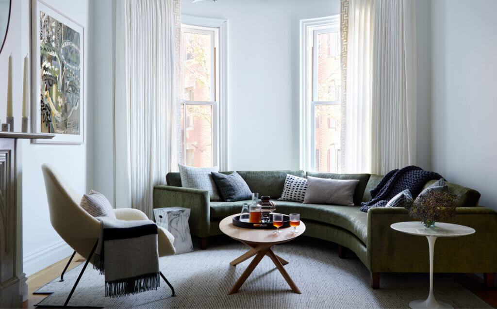 A Brownstone Interior Design project featuring a custom hunter green sofa, reupholstered white bouclé womb chair, and an oval coffee table.