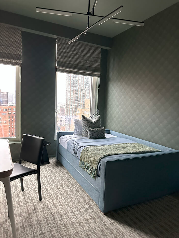 Boys' bedroom with dark green wallpaper, a light blue trundle bed, modern lighting, and a Room & Board area rug in a New York City apartment.