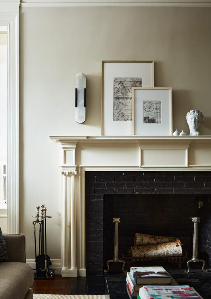 A formal living room with an original fireplace, freshly painted millwork, beige walls, simple art, and a modern light fixture from Kelly Wearstler.