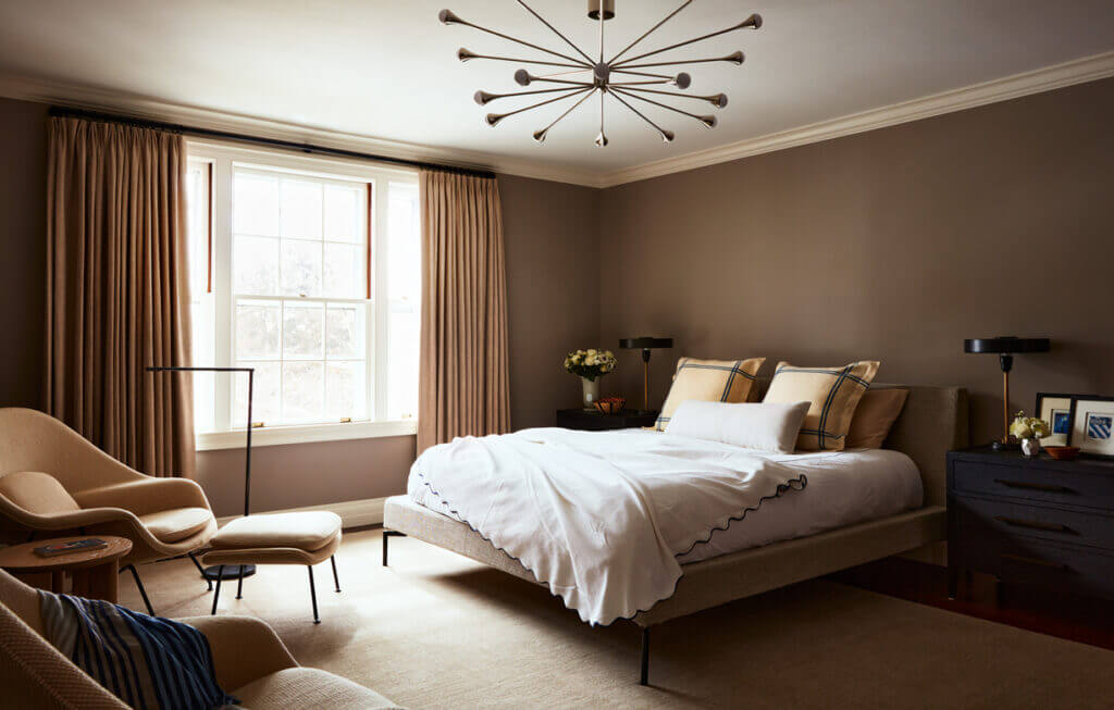 Historic Home Interior Design in a primary bedroom with a Blu Dot bed, black nightstands from Restoration Hardware, and neutral woven wool upholstered Womb chairs.