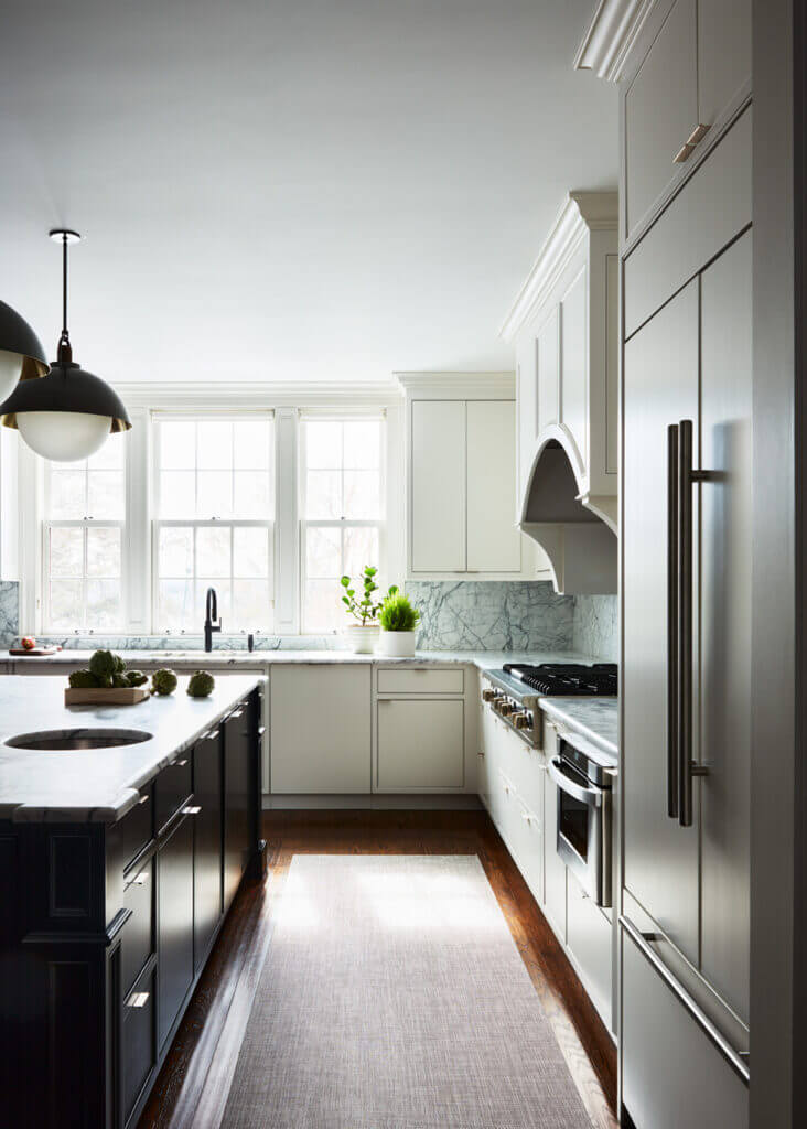 A modern kitchen with white slab doors, black island with marble counters, and black and brass fixtures hanging above for a striking contrast.