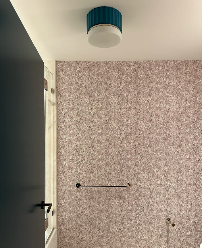 Schumacher feather-patterned wallpaper with a white and light brown pattern, accented by an aqua light fixture in a modern bathroom.