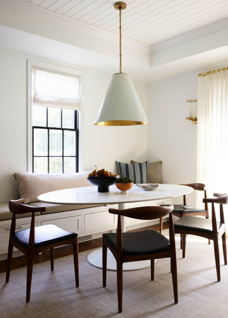 A modern dining room design with a Saarinen-inspired table, walnut and black chairs, a custom bench, and a brass pendant in a historic home.