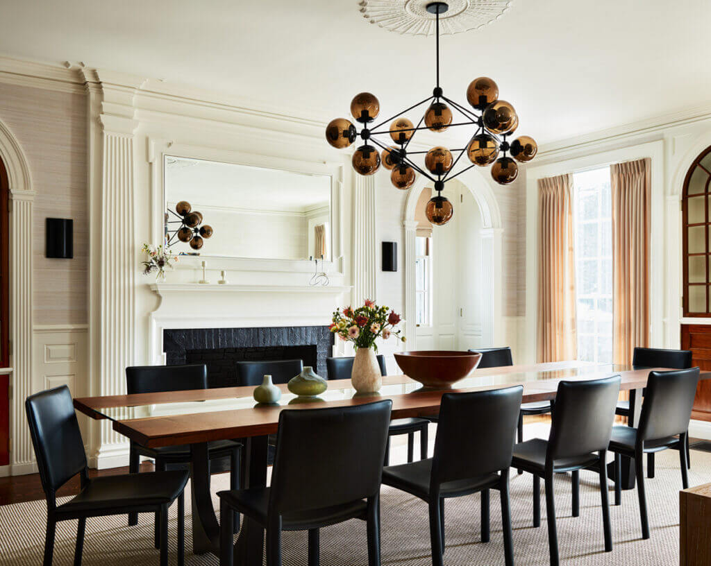 Historic Home Interior Design in a classic dining room with traditional wainscoting, elaborate fireplace details, sleek modern light fixtures, and a custom walnut and glass dining table with black leather chairs.