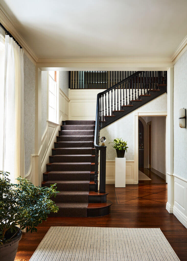 Historic Home Interior Design featuring a grand black-painted staircase with neutral wallcovering, freshly painted millwork, and a new stair runner in a historic Concord home foyer.