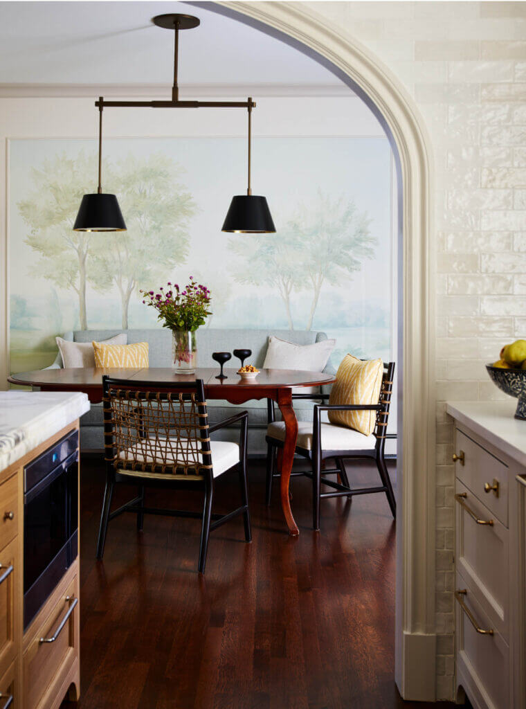 A classic dining room design with a vintage table, woven Palacek chairs, a blue sofa under a Susan Harter mural, and Urban Electric lighting.