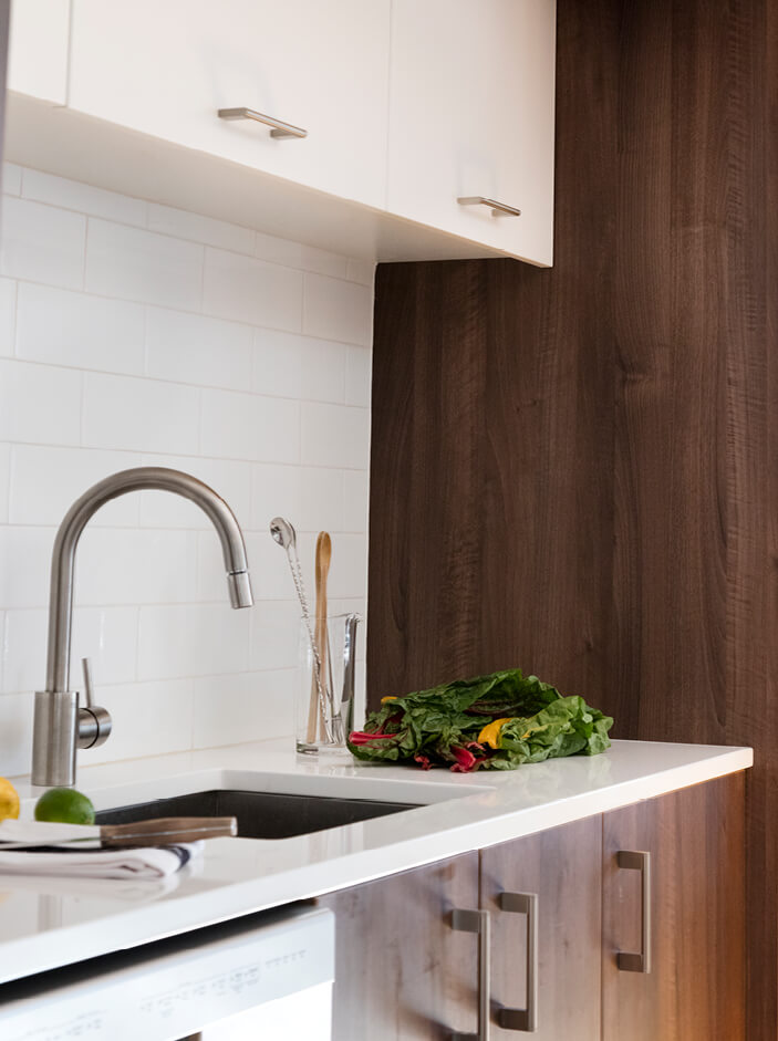 A South Boston loft kitchen with walnut and white cabinets, a modern faucet, white counters, and a clean white tile backsplash.