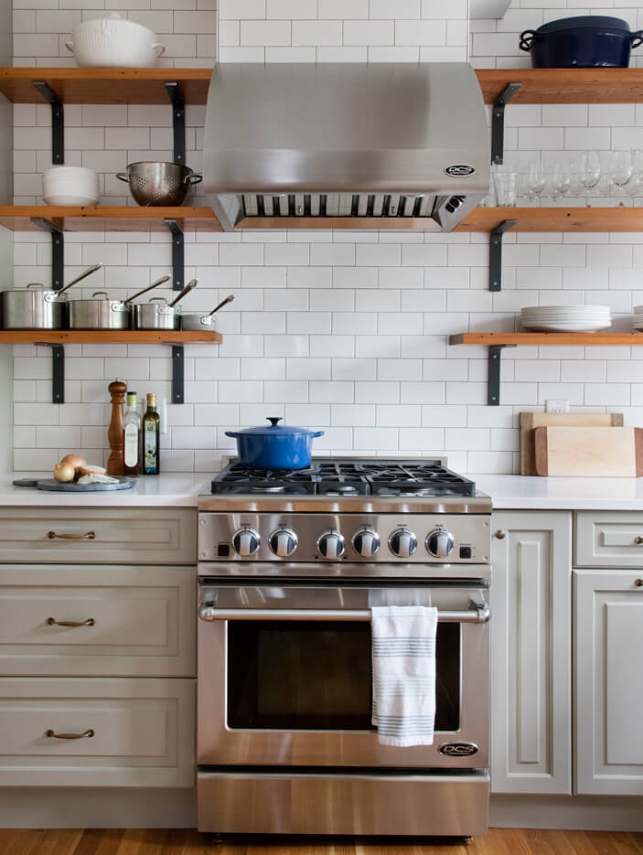 A vintage-inspired Boston kitchen design in Winchester with light green cabinets, reclaimed wood shelves, and a professional range and hood.