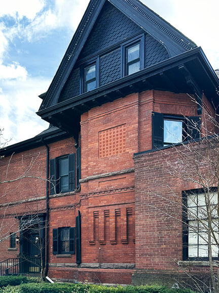 Historic red brick home in Toronto with black attic roofline and detailed wood trim, located in the Annex neighborhood
