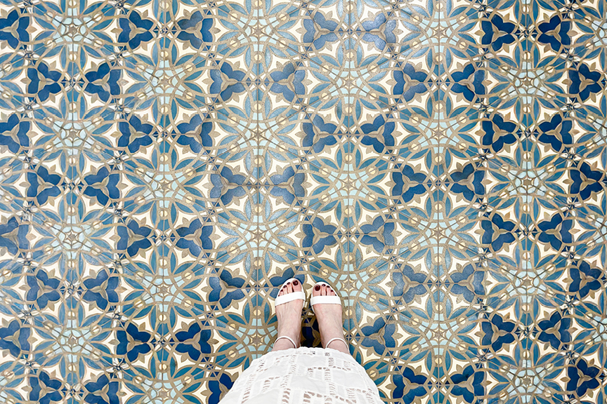 Sarah Flint shoe review with white block sandals and embroidered skirt on colorful Mediterranean hexagon tile in blue, green, and white.