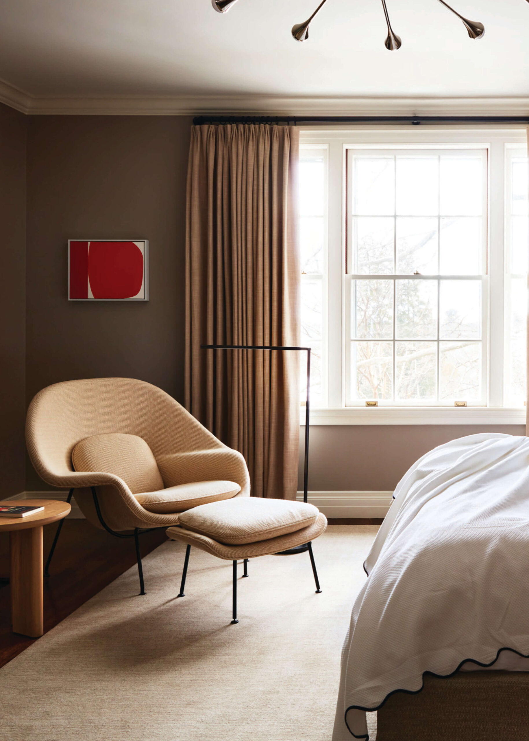 Cozy bedroom in a historic Concord home with womb chair, soft rug, drapery panels, and upholstered bedding.
