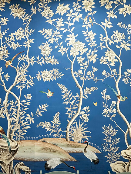 LA interior design showrooms include Gracie’s bright blue hand-painted wallpaper with white flowers and birds in a detailed floral pattern