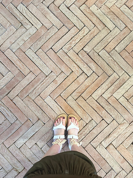 Boston interior designer captures Sarah Flint’s white Grear sandal in wrap-up style on hand-laid unglazed terracotta herringbone tile.