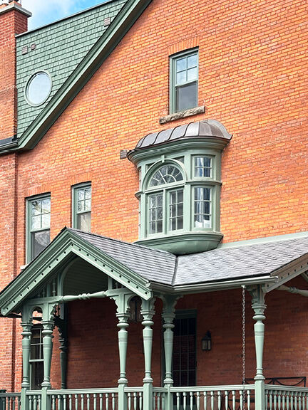 Queen Anne Revival home in Toronto’s Annex with red brick exterior, curved bay window, and intricate Victorian woodwork details