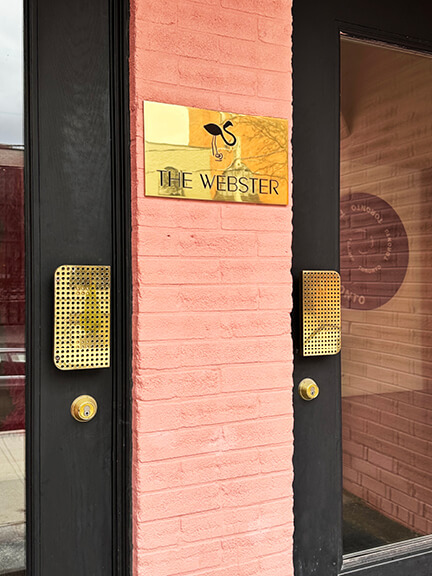 Pink-painted historic brick building in Yorkville, Toronto, featuring brass door hardware and black-painted doors at The Webster boutique