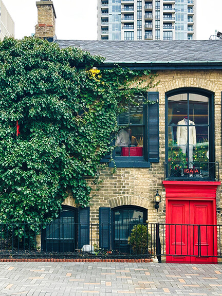 Historic yellow brick building in Toronto with a bright red door and ivy-covered facade, home to Isaia's modern retail space in a preserved structure