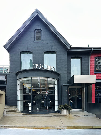 Charcoal-painted facade on a renovated historic brick building in Toronto’s Yorkville, featuring a curved window and modern retail interior design