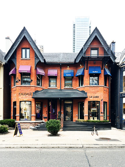 Semi-detached Victorian retail building in Yorkville, Toronto, featuring black-painted trim, a slate roof, and modern brands within a historic brick shell