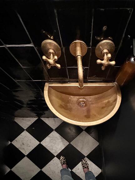 Historic-home-design-inspiration seen in Manita’s bathroom with a checkered floor, brass sink, and classic styling in Toronto.