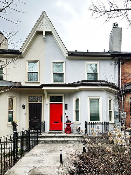 Red door on a painted brick semi-detached home in Toronto, showing subtle historic details and a crisp exterior palette.