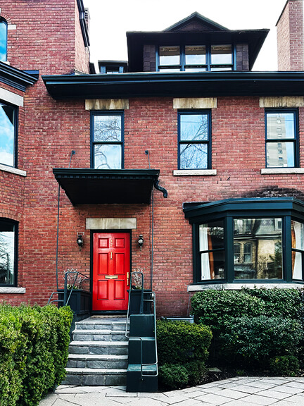 Classic red door and black accents on a historic brick home in Toronto, featuring simple symmetry and traditional details.