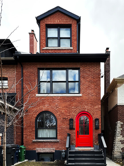 Red front door with black trim on a historic Toronto brick home, showcasing bold accents and preserved architectural lines.