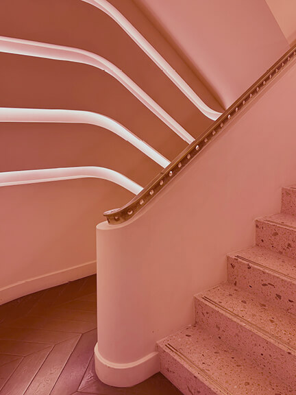 Modern pink staircase with terrazzo steps, herringbone flooring, plaster detailing, and integrated LED lighting inside a historic Toronto retail building