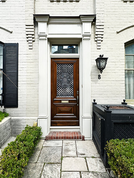 Historic-home-design-inspiration seen in white-painted brick, wood door with glass, and iron fixture at a Toronto entry.